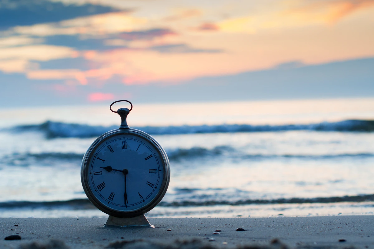 Reloj de bolsillo en la playa al atardecer, simbolizando el seguro de vida y la caducidad de esta.