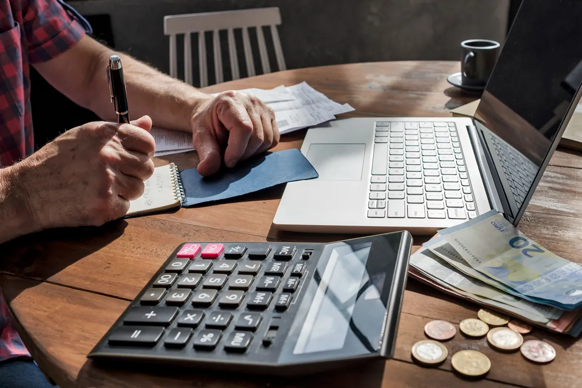 Hombre calculando el IRPF en una mesa, con una calculadora, un ordenador portátil y una libreta, siguiendo un ejemplo del régimen de estimación directa simplificada.